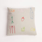 Neutral linen cushion with colourful embroidered food and drink icons on a white background.